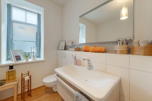 A modern bathroom with a large white sink, a toilet, and a window with blinds.
