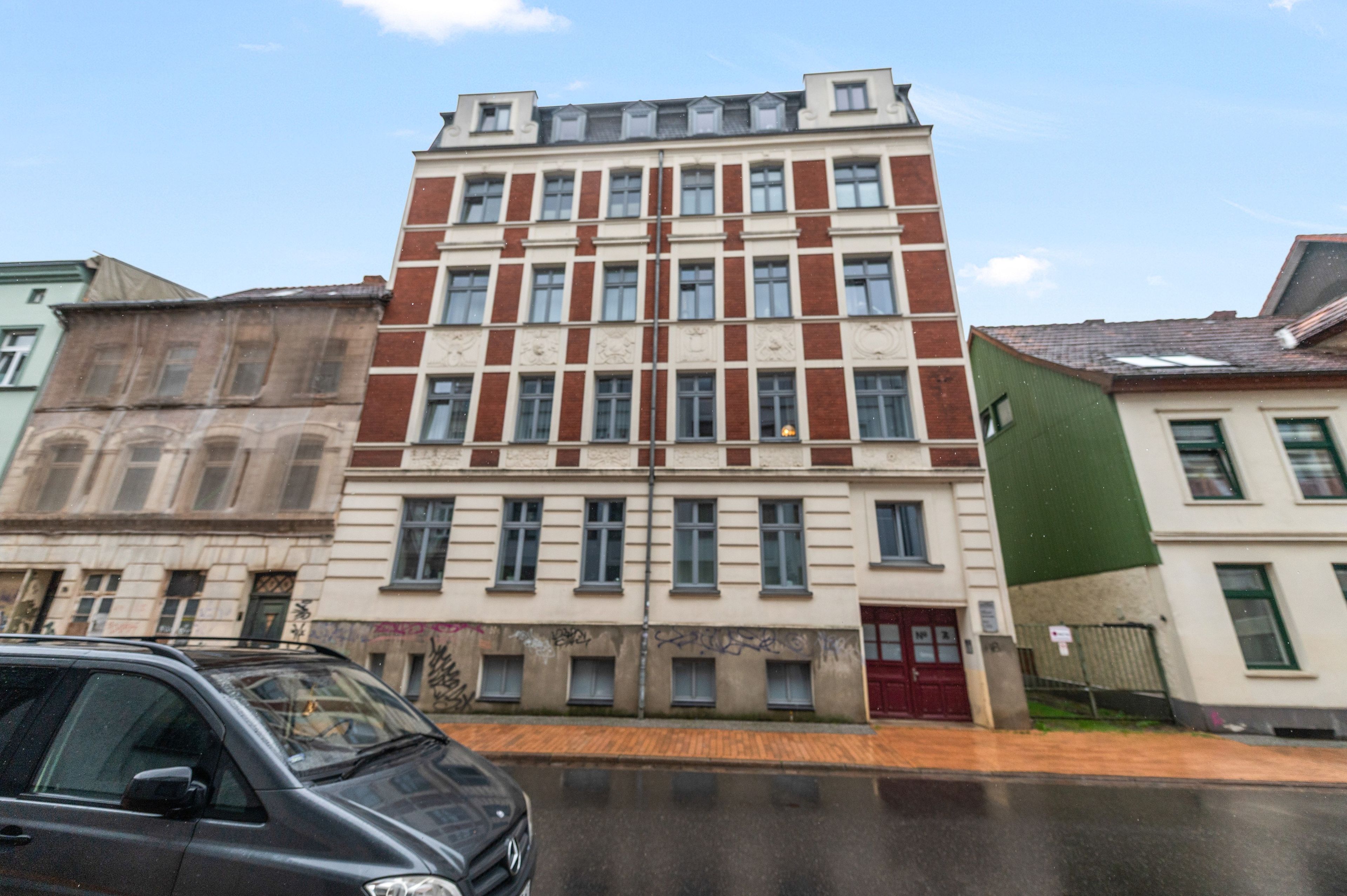 Un edificio de varios pisos con fachada simétrica, ventanas grandes y una puerta roja al nivel de la calle.