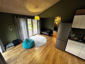 Un espacio habitable compacto con kitchenette, un asiento tipo bean bag y una puerta corredera de vidrio que da a un área exterior.