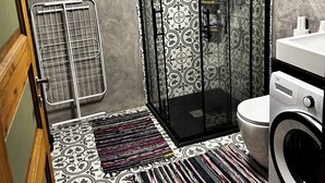 Casa de banho compacta com chuveiro, sanita e máquina de lavar roupa.