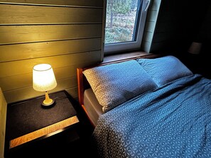 Una habitación con una cama, una mesita de noche con lámpara y una ventana.