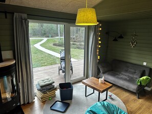 A cozy living room with a sofa, a coffee table, a television, and a view of a garden through a sliding glass door.