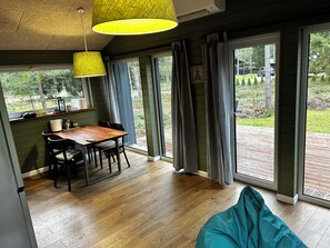 A modern interior with a wooden dining table, chairs, a yellow hanging light, and large sliding glass doors leading to an outdoor deck.