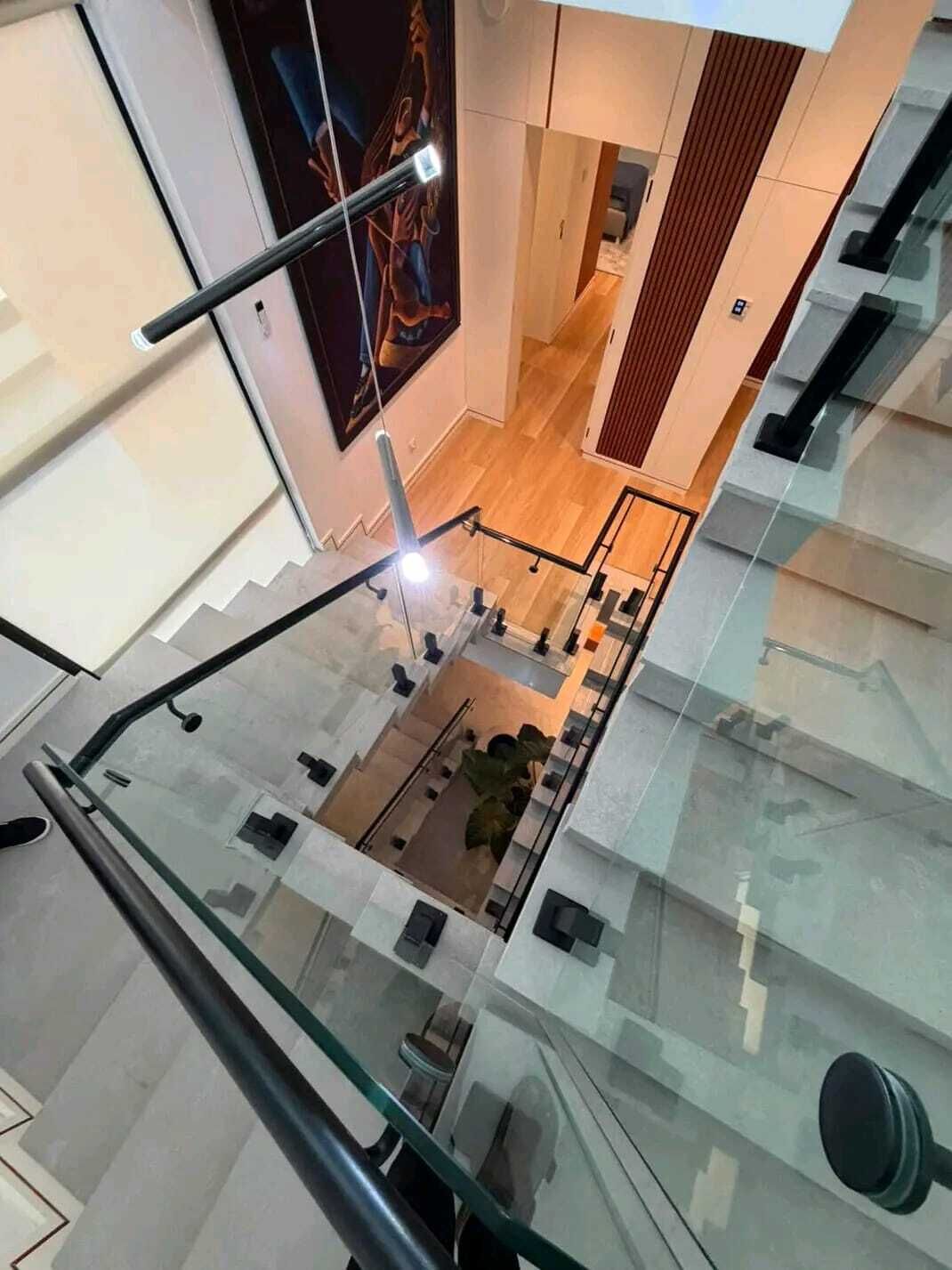 A modern interior with a glass railing, a staircase, and a view of a dining area below.