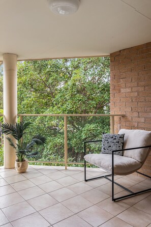 Un balcon avec une chaise, un pot de fleurs et une vue sur la verdure.