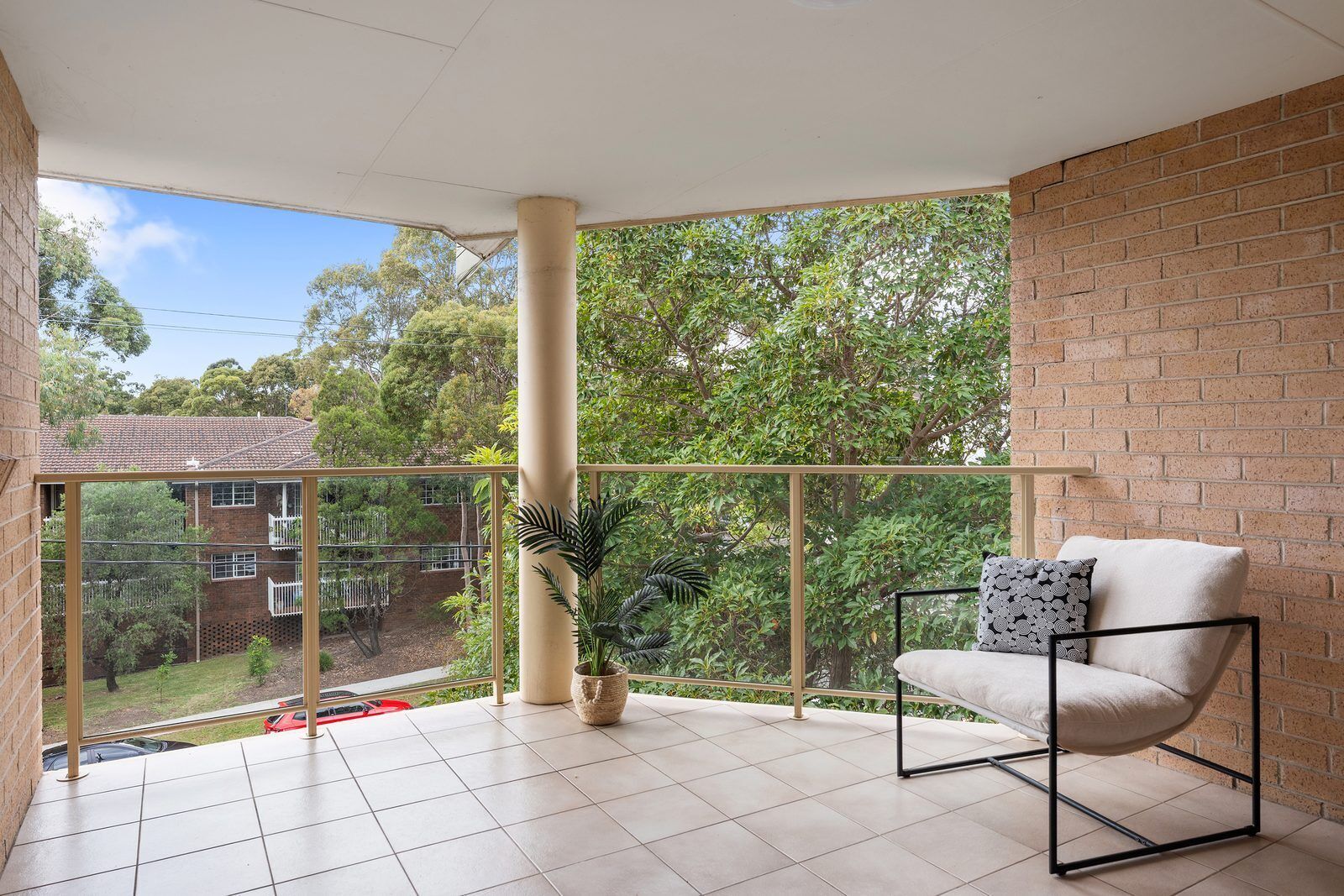 A balcony with a chair, a potted plant, and a view of a residential area.