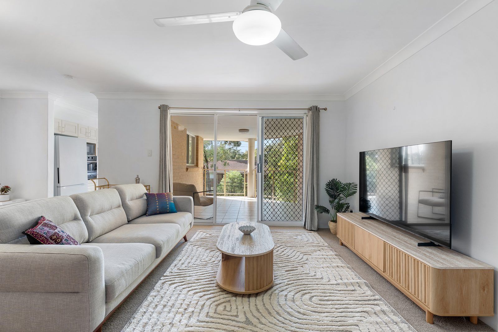 A modern living room with a sofa, coffee table, TV, and a view to the outside.