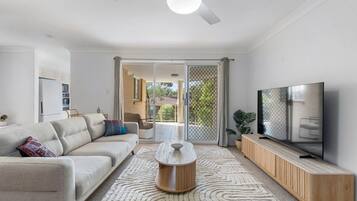 A modern living room with a sofa, coffee table, TV, and a view to the outside.