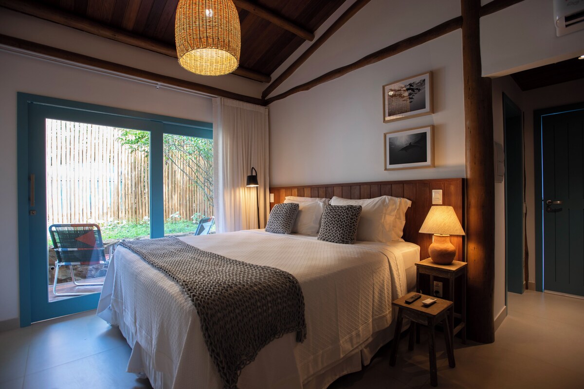 A bedroom with a large bed, a bedside table with a lamp, a window with curtains, and a door.