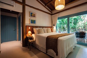 A bedroom with a bed, bedside table, lamp, and a view of greenery outside. - POUSADA VEREDAS NORONHA (Fernando de Noronha)
