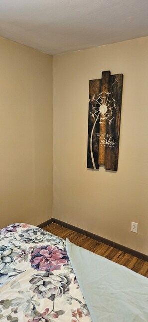 A bedroom with a floral bedspread, a wooden wall art piece, and a wooden floor.