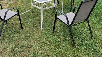 Un patio con una mesa de metal y dos sillas, una valla de madera, y una casa al fondo.