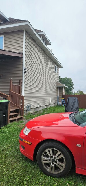 A red car parked in a grassy yard with a house in the background.
