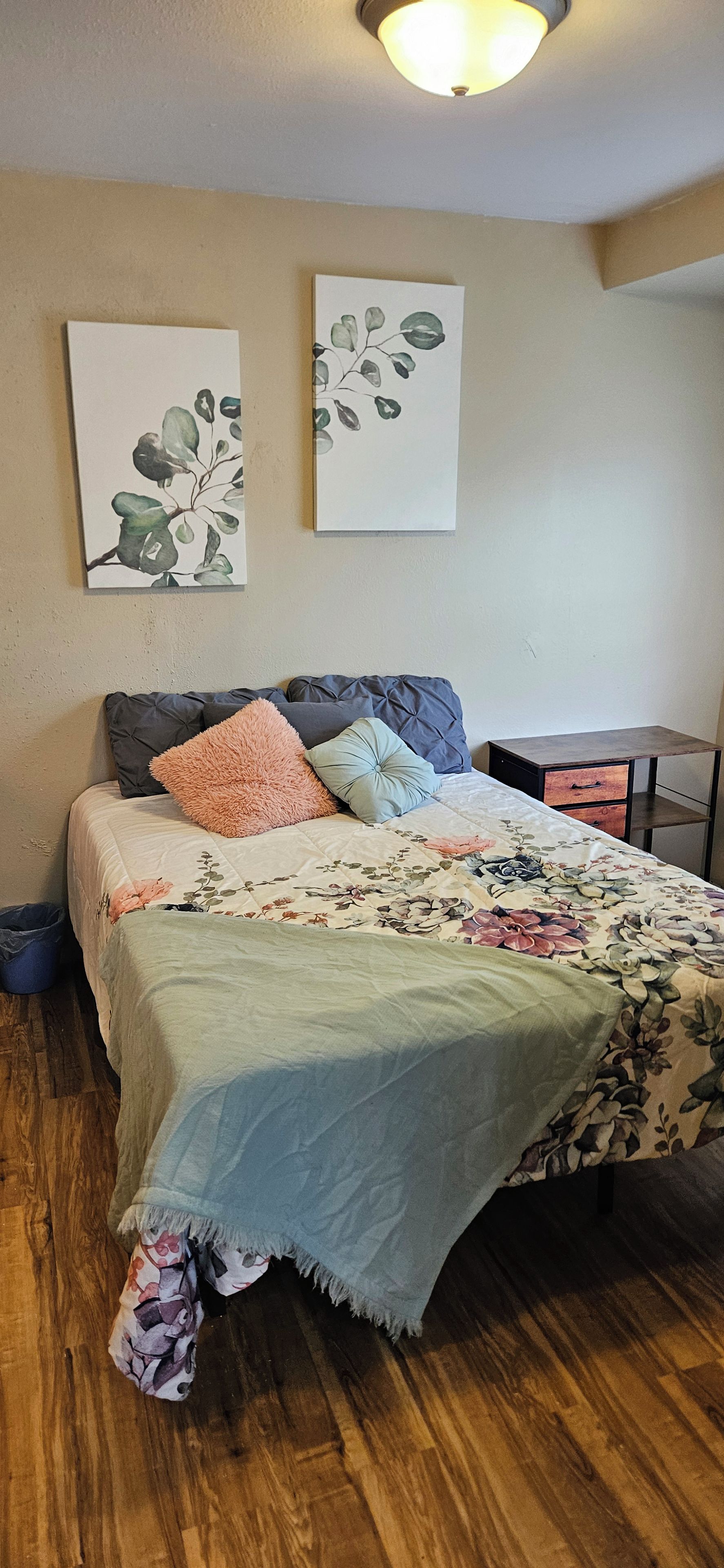 A bedroom with a bed, a nightstand, a dresser, and two wall-mounted paintings.