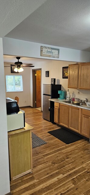A kitchen with wooden cabinets, a refrigerator, a coffee maker, and a ceiling fan.