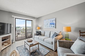 A living room with a television, a sofa, a coffee table, and a painting on the wall. - Coastal Condo 2 bedroom• Pool • Steps to Beach (North Myrtle Beach)