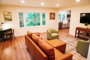 A living room with a sectional sofa, a green armchair, a TV, and a kitchen in the background. - Modern Mountain Cottage Near Downtown Spruce Pine, NC (Spruce Pine)