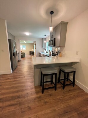 A modern kitchen with a central island, two stools, and a dining area in the background. - Modern Mountain Cottage Near Downtown Spruce Pine, NC (Spruce Pine)