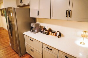 Une cuisine équipée d’un réfrigérateur en acier inoxydable, d’une machine à café, d’une petite horloge et d’une lampe sur le plan de travail.