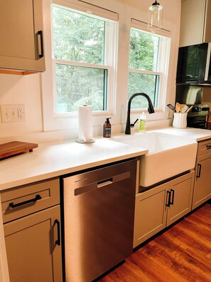 A kitchen with a dishwasher, a sink, and a window overlooking greenery. - Modern Mountain Cottage Near Downtown Spruce Pine, NC (Spruce Pine)