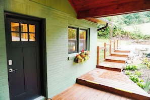Une maison avec une porte d’entrée sombre, une fenêtre agrémentée d’une jardinière et un escalier en bois menant à un porche.