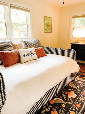 A bed with a white comforter and multiple pillows, a black and white checkered headboard, and a floral-patterned rug. - Modern Mountain Cottage Near Downtown Spruce Pine, NC (Spruce Pine)