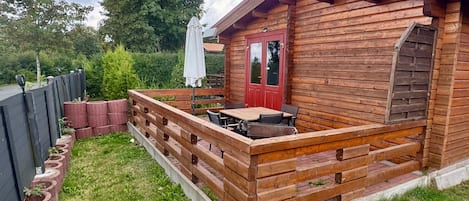 Une cabane en bois avec une terrasse, une porte rouge et une petite table entourée de chaises.