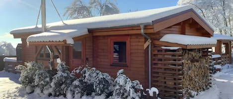 A wooden cabin with a snow-covered roof, a window, and a door.