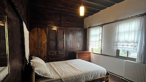 Una stanza con struttura in legno, un letto, una cassettiera e una finestra con tende.
