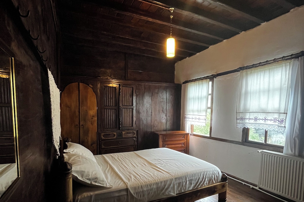 Una stanza con struttura in legno, un letto, una cassettiera e una finestra con tende.
