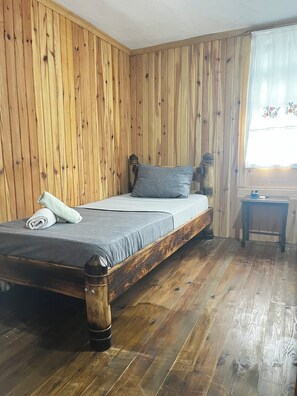 A wooden-paneled room with a bed, a small table, and a window with curtains. - Uzunhasanoğlu Konağı (Findikli)