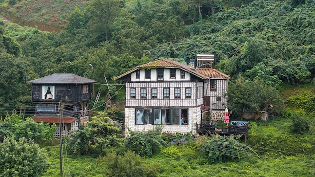 Una casa tradizionale con struttura a graticcio e un balcone, immersa nel verde.