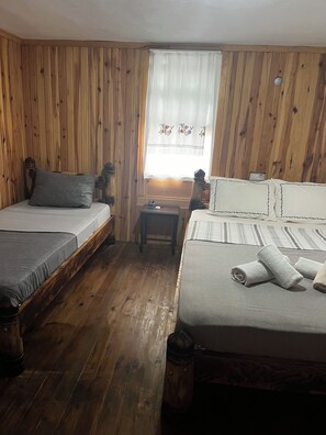 A room with two beds, wooden walls, a small table, and a window with curtains.