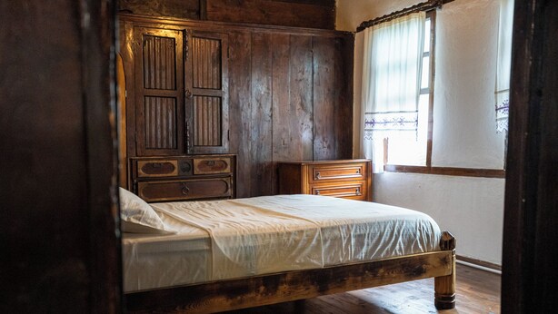 Una cama de madera con diseño sencillo, un aparador de madera y una ventana con cortinas.