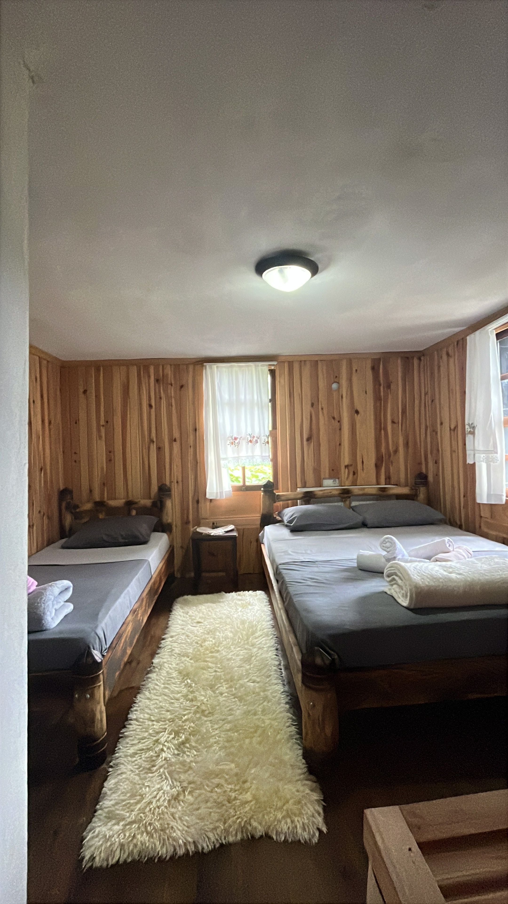 A room with two wooden beds, a white fluffy rug, and a ceiling light.