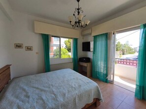 A bedroom with a bed, a desk, a television, and a balcony with curtains.