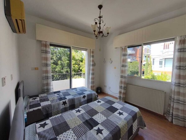 A bedroom with two beds, a radiator, a window with curtains, and a chandelier.