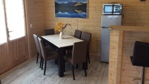Ein Essbereich mit Tisch, Stühlen, einer Blumenvase, einem Kühlschrank und einer Uhr an der Wand.