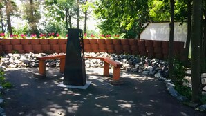 A paved area with a black sculpture, two wooden benches, and a stone wall with flowers.