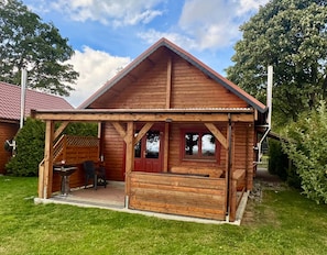 Une cabane en bois dotée d’un porche abrité, d’un coin repas avec des chaises et d’une fenêtre donnant sur les arbres environnants.