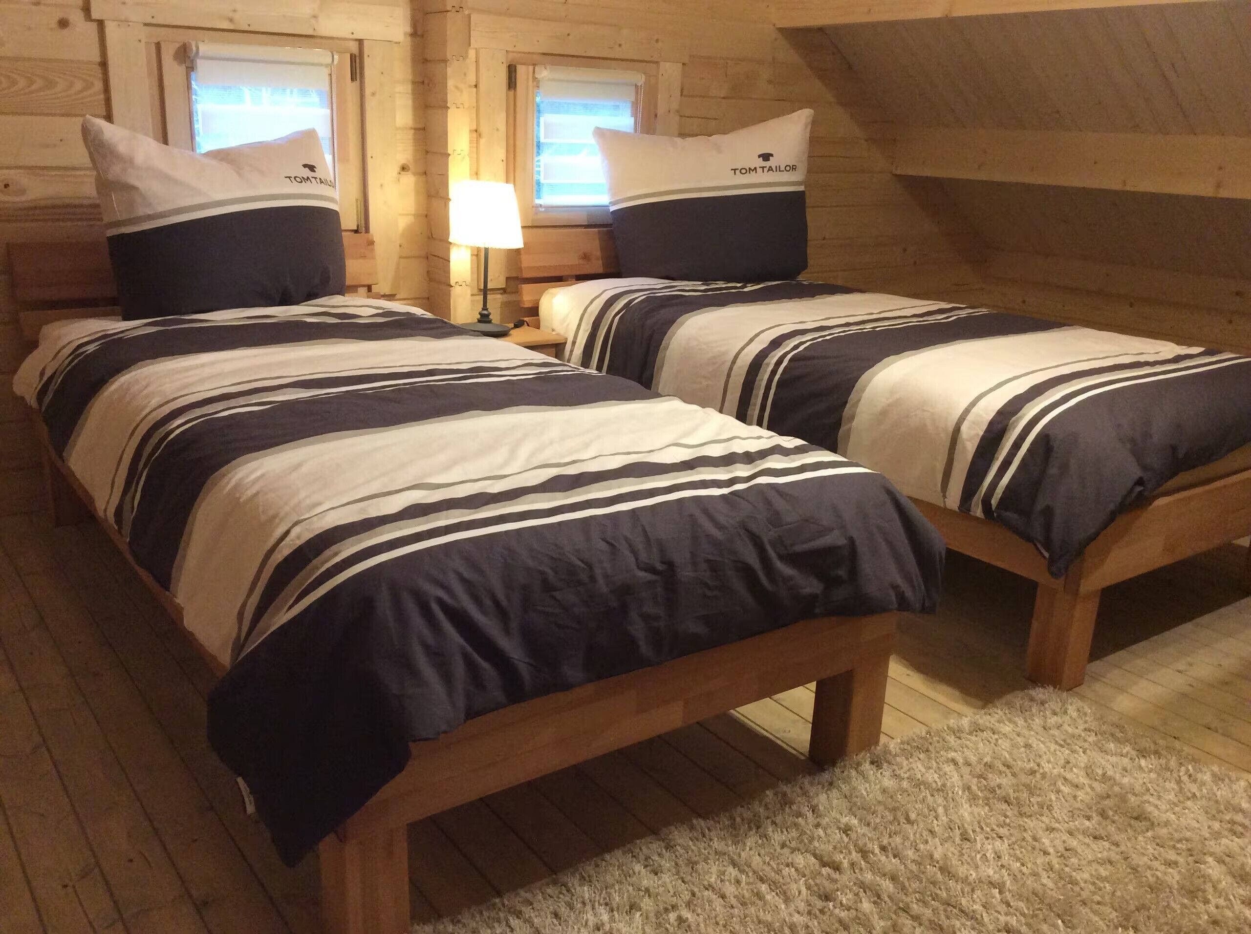 A room with two wooden beds, each with striped bedding and pillows labeled 'TOMTAILOR.'
