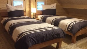 Ein Zimmer mit zwei Holzbetten, jeweils mit gestreifter Bettwäsche und Kissen mit dem Aufdruck 'TOMTAILOR'.