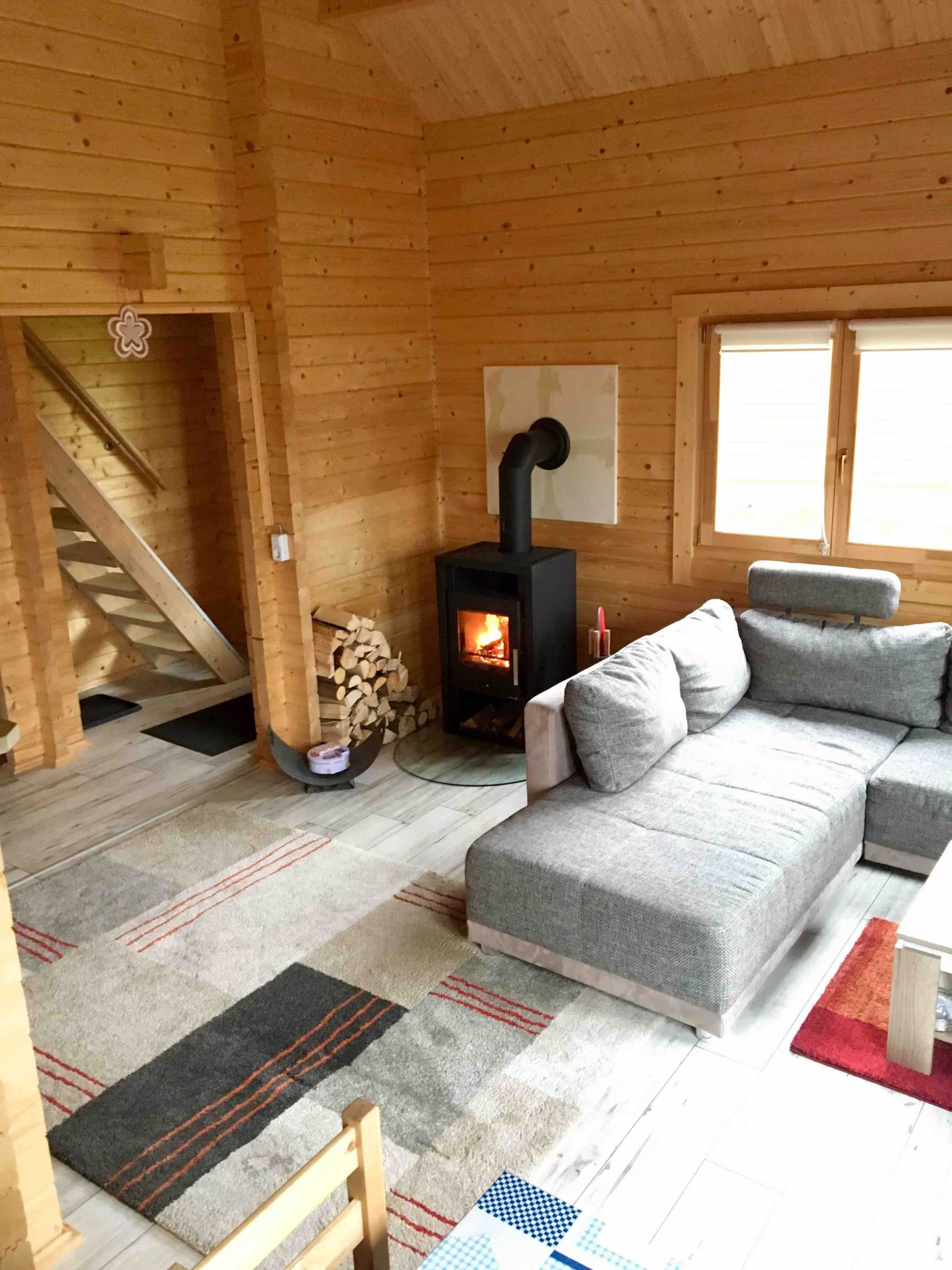 A cozy cabin interior with a sofa, a fireplace, a staircase, and a window.