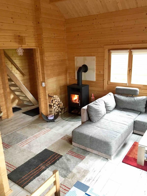 A cozy cabin interior with a sofa, a fireplace, a staircase, and a window. - Holiday Home 'Peak-Butze Hohegeiß Log Cabin Harz' with Balcony, Wi-Fi and Air Conditioning (Braunlage)