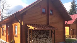 A wooden cabin with a covered porch, a stack of firewood, and a small window.