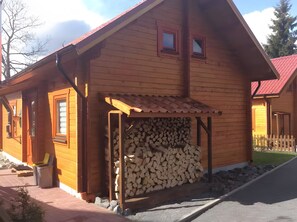 A wooden cabin with a covered porch, a stack of firewood, and a small window.