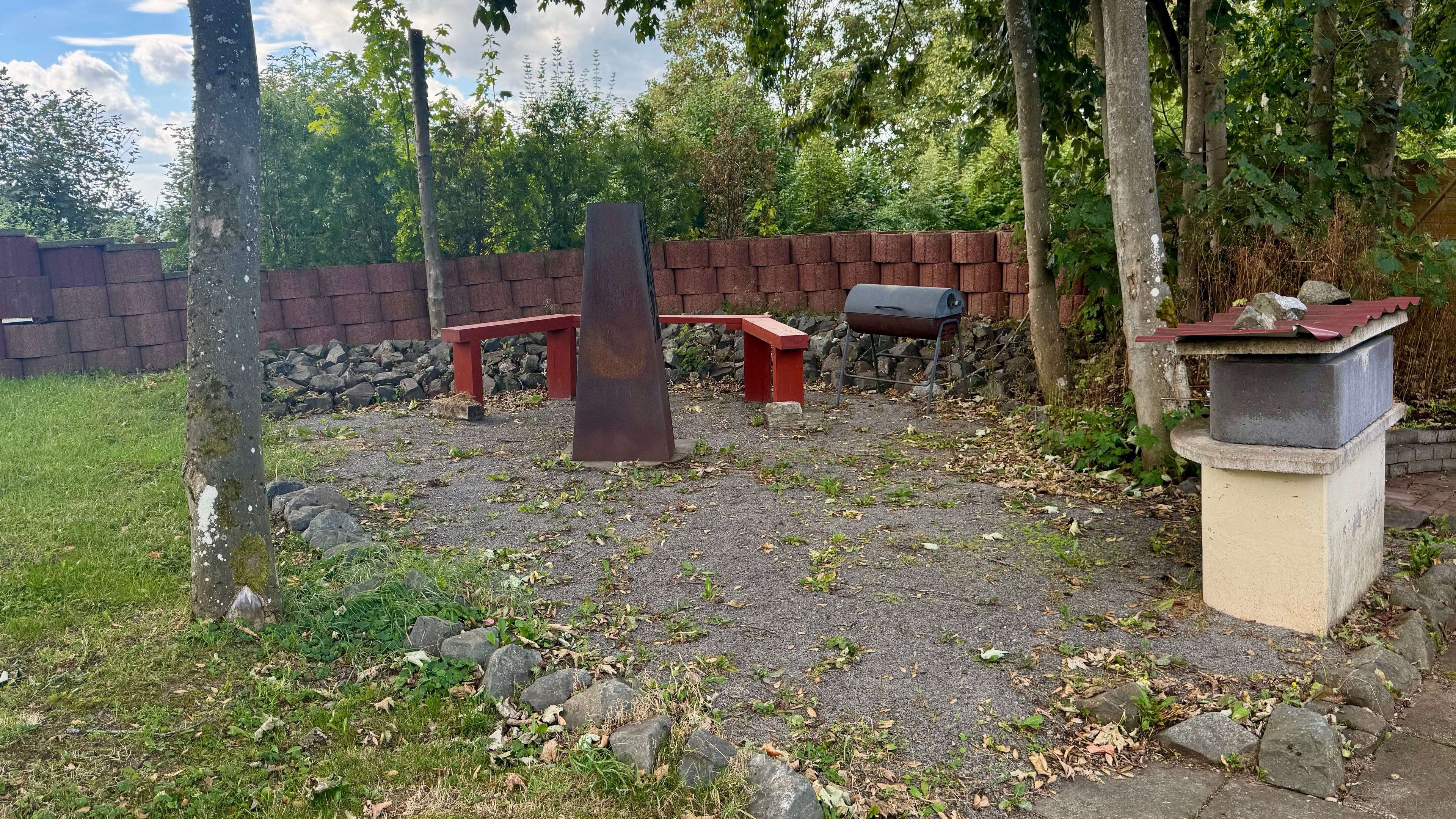 Ein Garten mit Grill, rotem Bank und Steinbauwerk.