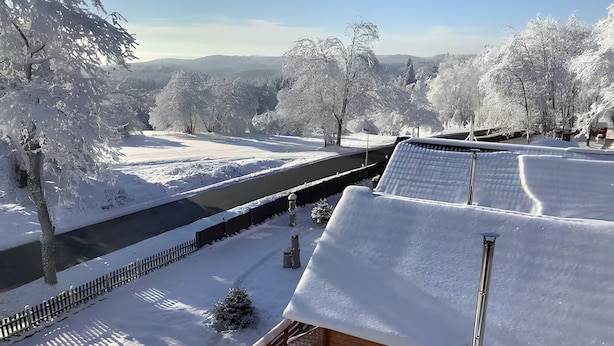 A snow-covered landscape with a wooden cabin and a bridge.