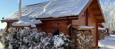 A wooden cabin with a snow-covered roof, a chimney, and a stone wall.