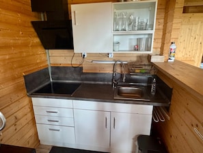 Une cuisine de taille réduite, dotée d’un évier en acier inoxydable, de meubles blancs et de murs en bois.